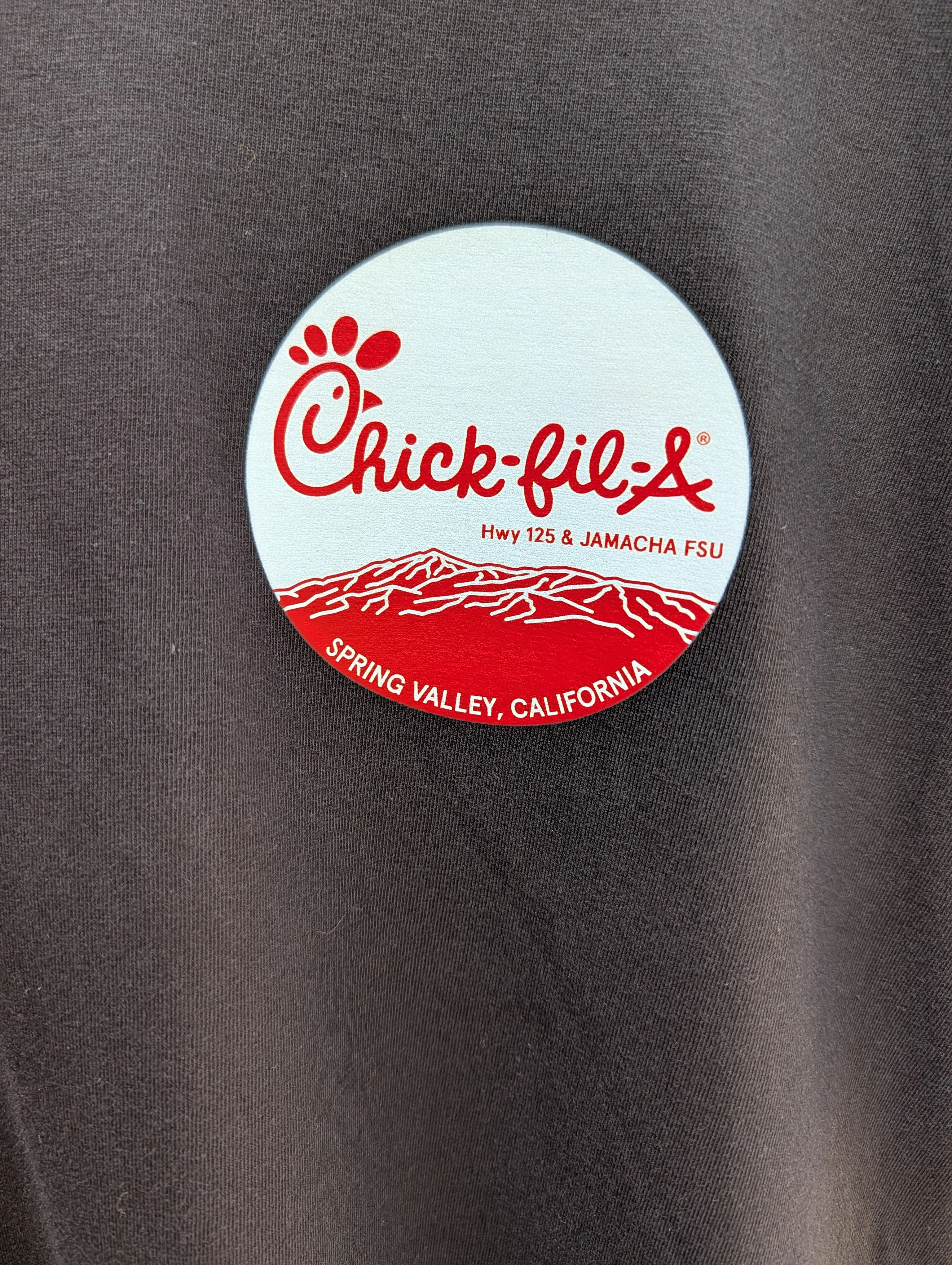 Close-up of the DTF-printed Chick-fil-A Spring Valley Hwy 125 & Jamacha circle logo on a black giveaway tee