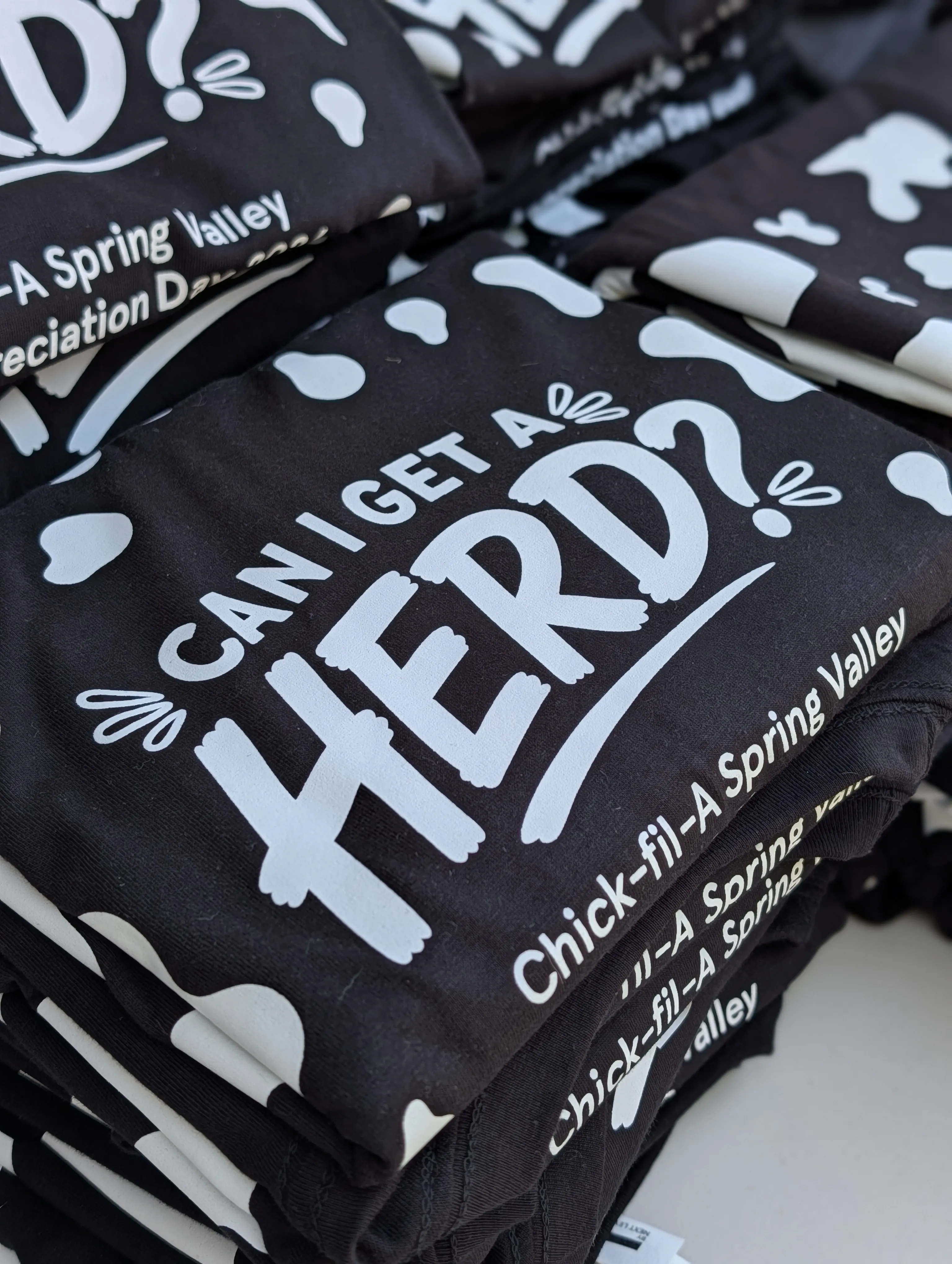Folded stacks of black screen-printed 'Can I get a herd?' staff tees ready for delivery